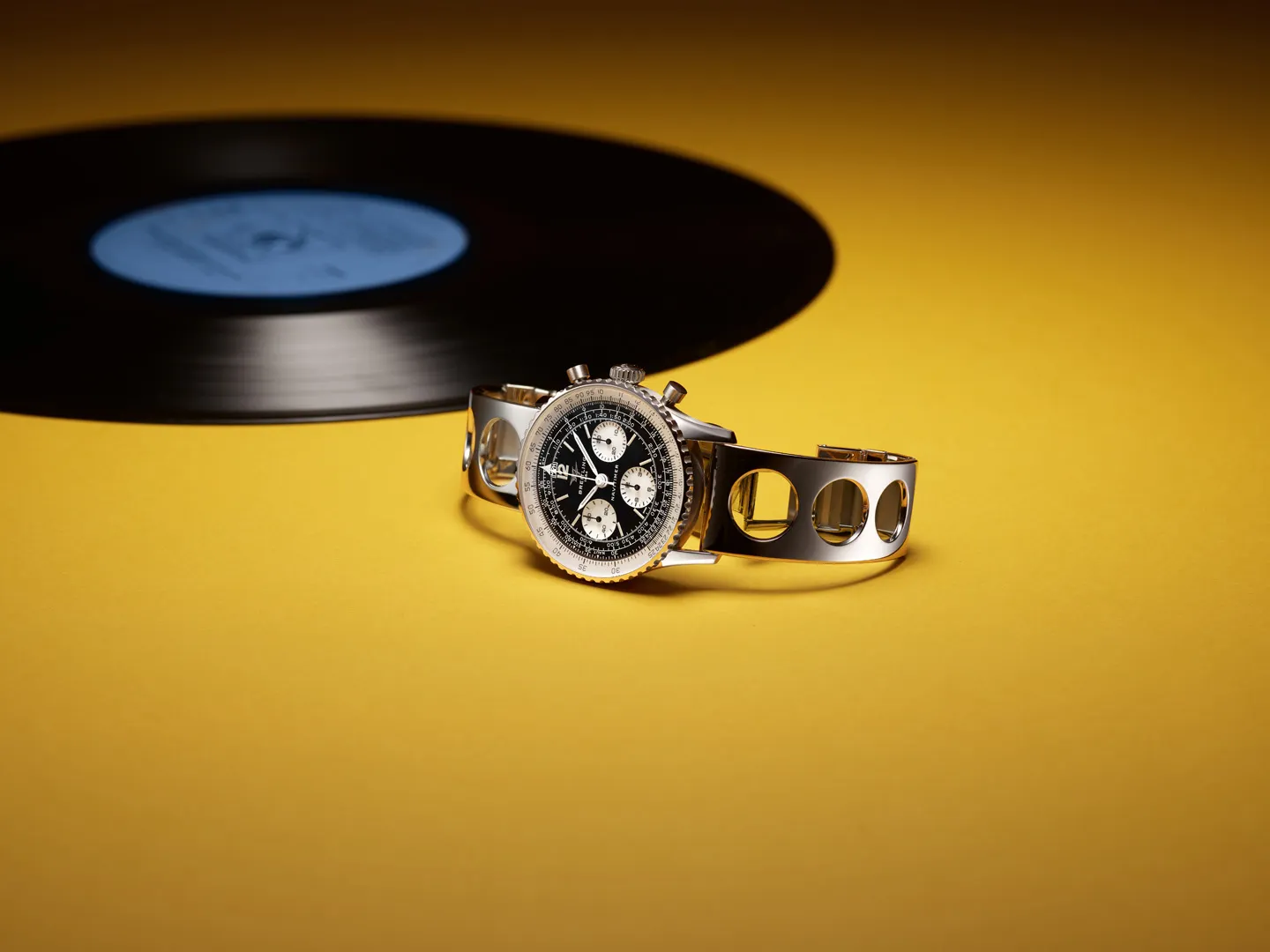 Breitling Navitimer B09 Chronograph 41 Tribute to Miles Davis ความพิเศษฉลอง 100 ปีนักดนตรีแจ๊สระดับโลก หน้าปัด Reverse Panda และโลโก้ Twin Jet ของ Breitling Navitimer B09 Chronograph 41 Tribute to Miles Davis บนพื้นสีเหลืองกับแผ่นเสียง